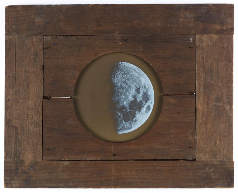 Magic lantern slide showing the Moon. A circular illustration of the Moon is shown at the centre of a wooden board